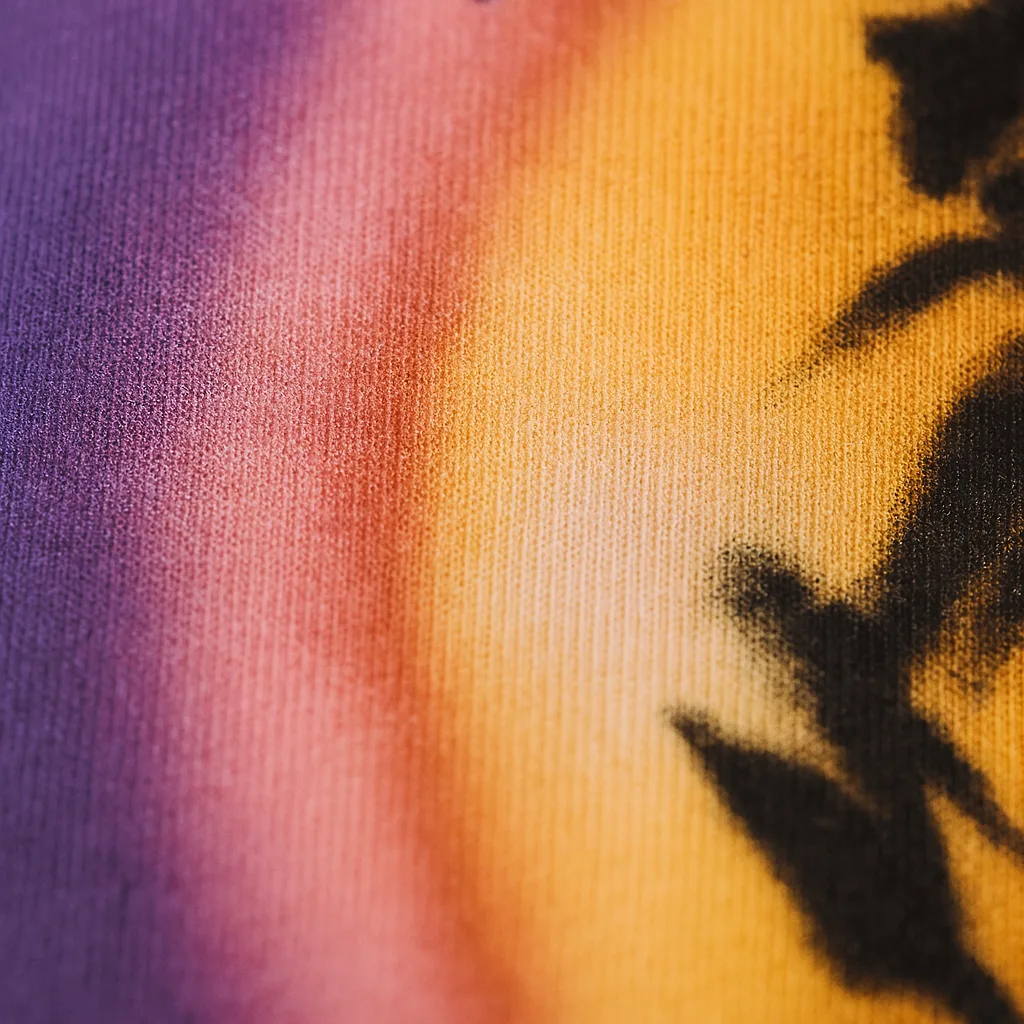 Extreme close-up of a DTF print on fabric showing a smooth gradient from purple to golden yellow with visible pigment dots and raised texture