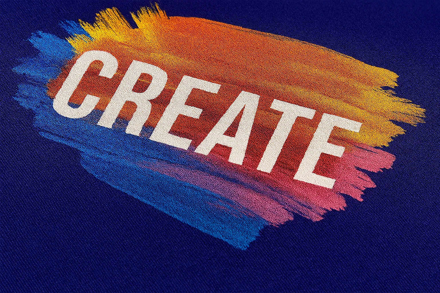 Close-up of a printed t-shirt with the word “CREATE” in white, surrounded by vibrant brushstroke colors on purple fabric.