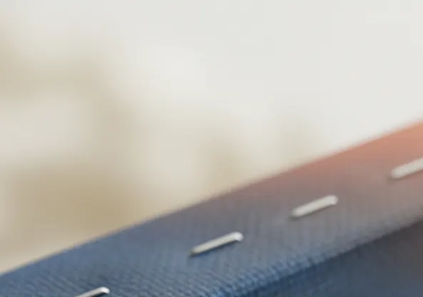 A macro photograph showing a close-up of a wooden stretcher bar and the stapled edge of a canvas print, revealing the texture of the canvas, the neatly placed staples, and the clean edge of the wood.